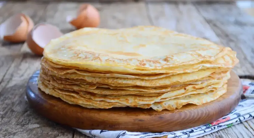 Pila di crepes dorate, perfette per una crepes ricetta senza burro. Guscio d'uovo sullo sfondo.