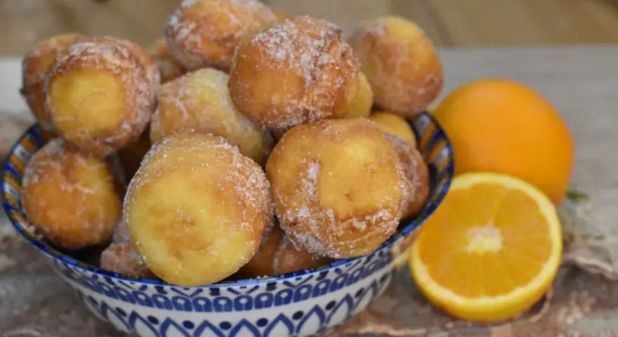 Arancini dolci, soffici arrubiolus di ricotta cosparsi di zucchero, accanto a fette d'arancia.