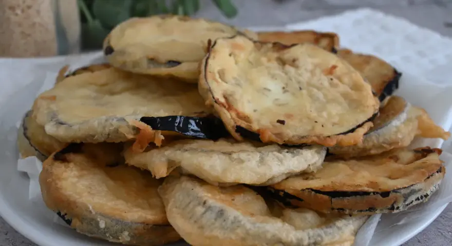 Piatto di melanzane fritte pastellate, dorate e croccanti, pronte per essere gustate.