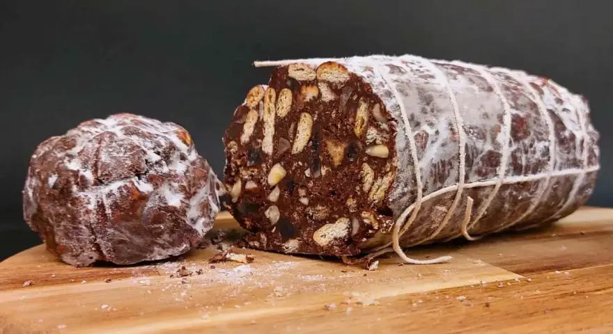 Salame al cioccolato vegano, un dolce goloso con biscotti e frutta secca, spolverato di zucchero a velo.