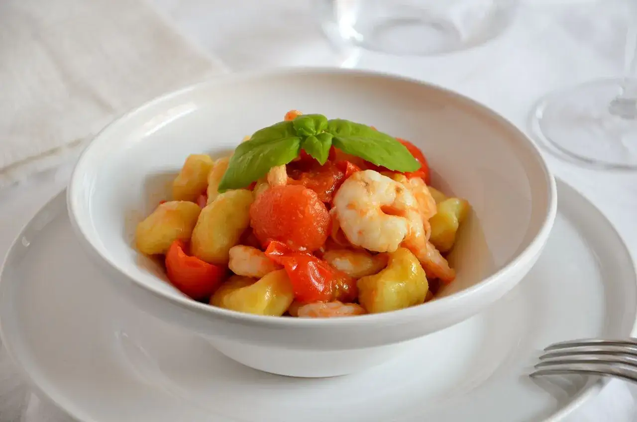 Gnocchi con gamberi e pomodorini freschi, guarniti con basilico. Un piatto di pasta leggero e saporito.