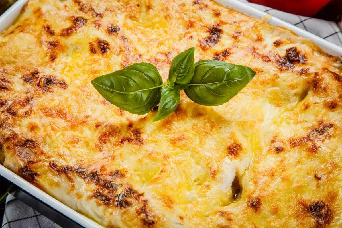 Piatto fumante di pasta con melanzane in bianco cremosa, gratinata al forno e guarnita con foglie di basilico fresco.