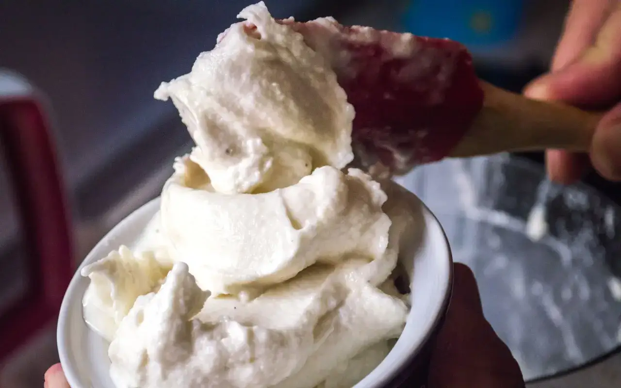 Una spatola rossa serve un cremoso gelato fatto in casa in una ciotola bianca.