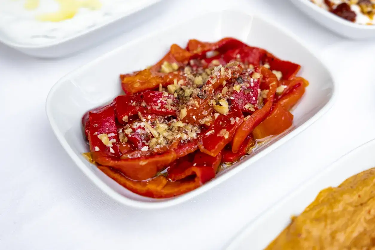 Peperoni rossi arrostiti, conditi con aglio e noci, serviti in un piatto bianco. Un'idea veloce per peperoni al microonde.