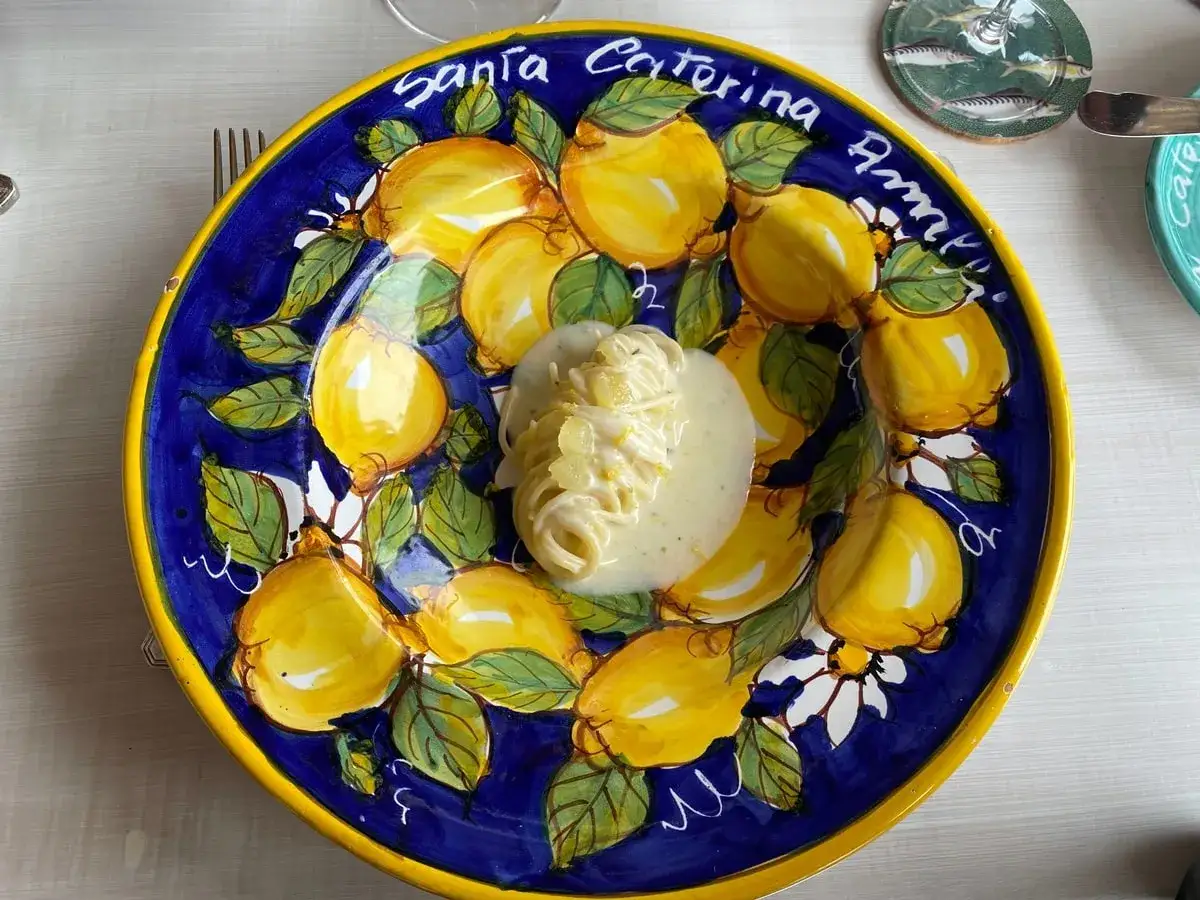 Spaghetti al limone, ricetta della Costiera Amalfitana, serviti su un piatto dipinto con limoni e fiori.