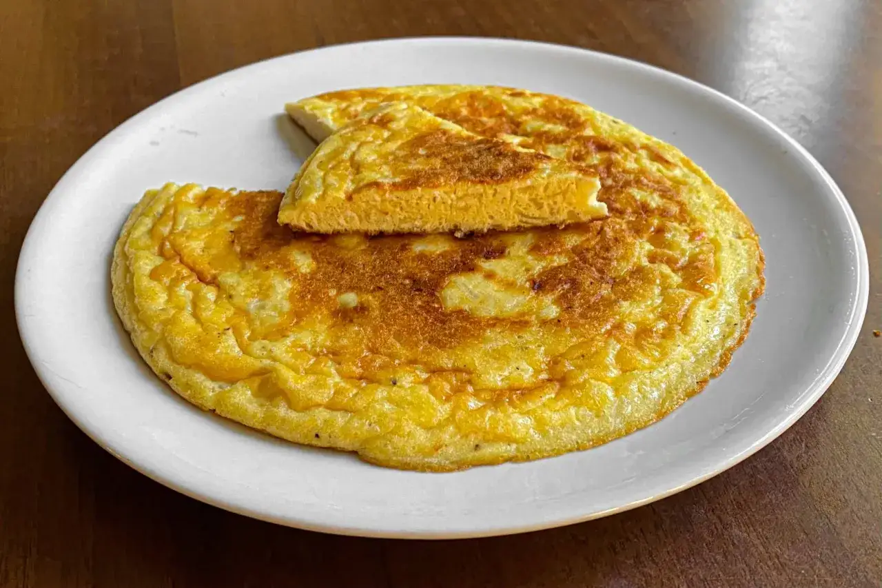Una dorata frittata di cipolle, soffice e invitante, servita su un piatto bianco.