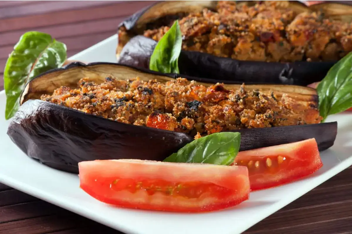 Melanzane a barchetta ripiene, guarnite con basilico fresco e fette di pomodoro, pronte per essere gustate.