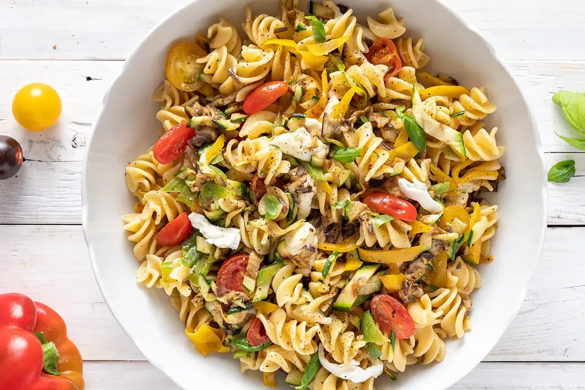 Un piatto invitante di pasta fredda vegana con fusilli, pomodorini, zucchine, peperoni gialli e basilico fresco.