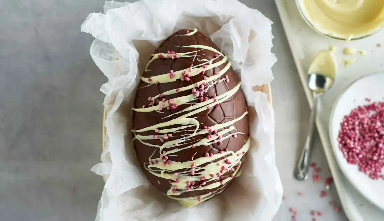 Un magnifico uovo di Pasqua fatto in casa, ricoperto di cioccolato fondente, decorato con glassa bianca e granella rosa.
