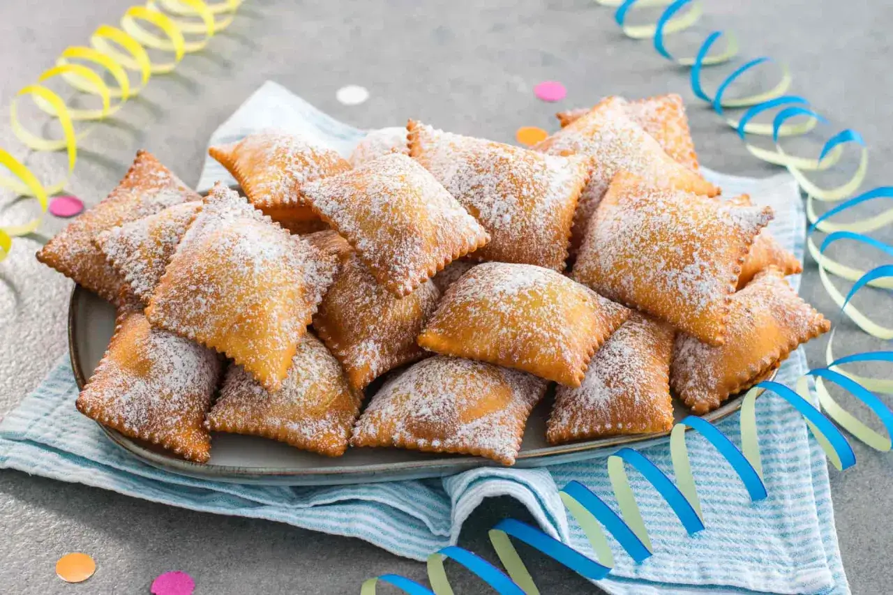 Piatto di bugie ricetta originale, dolci fritti cosparsi di zucchero a velo, con festoni colorati sullo sfondo.