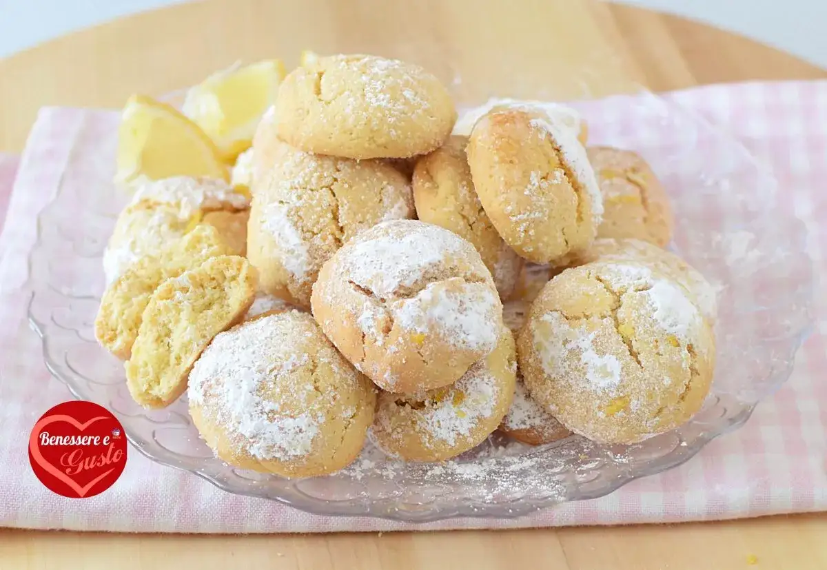 Biscotti alla ricotta spolverati di zucchero a velo, con scorza di limone e spicchi freschi.