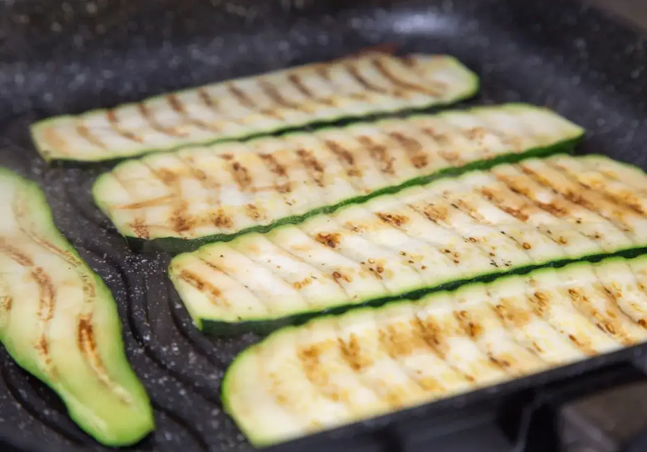 Fette di zucchine grigliate sulla piastra, con striature dorate e bordi verdi freschi.