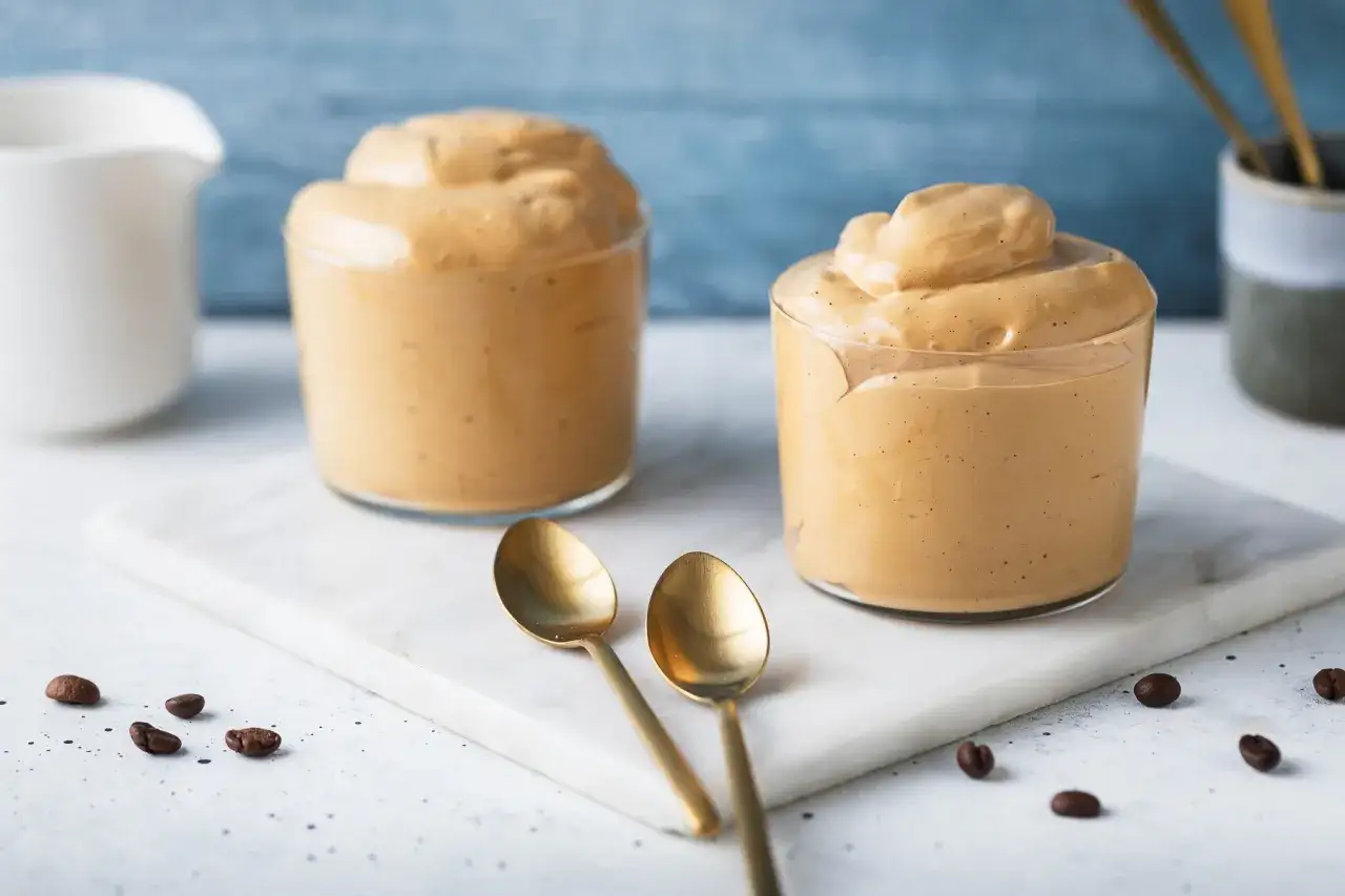 Due bicchieri di cremosa schiuma di caff&egrave;, perfetta per una ricetta crema di caff&egrave; senza panna. Due cucchiaini dorati e chicchi di caff&egrave; completano la scena.
