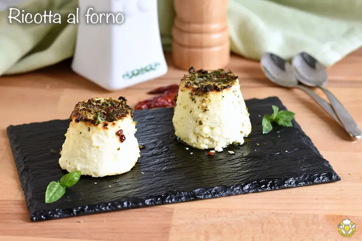 Due tortini di ricotta al forno, dorati e profumati, serviti su ardesia con basilico e peperoncino.