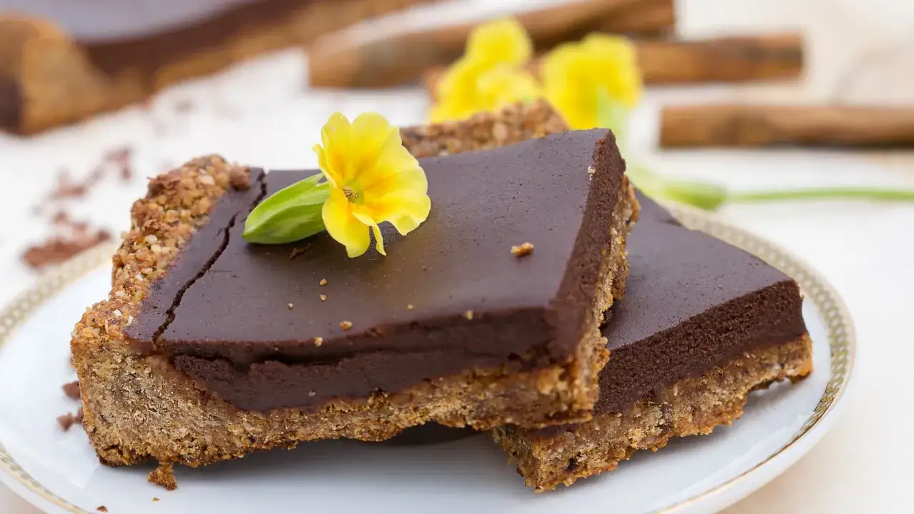 Fette di torta al cioccolato con base croccante, guarnite con un fiore giallo e un tocco di crema al cocco.