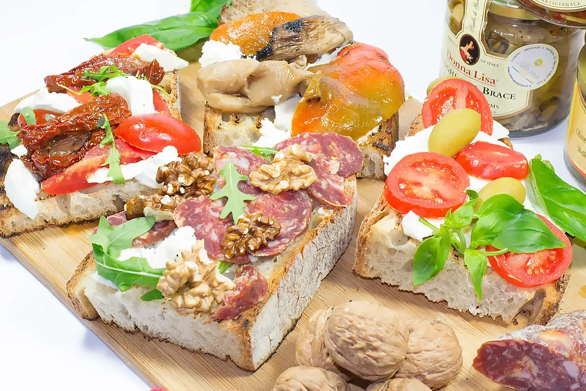 Bruschette veloci per aperitivo: pane tostato con pomodori secchi, mozzarella, salumi, noci, verdure grigliate e olive.