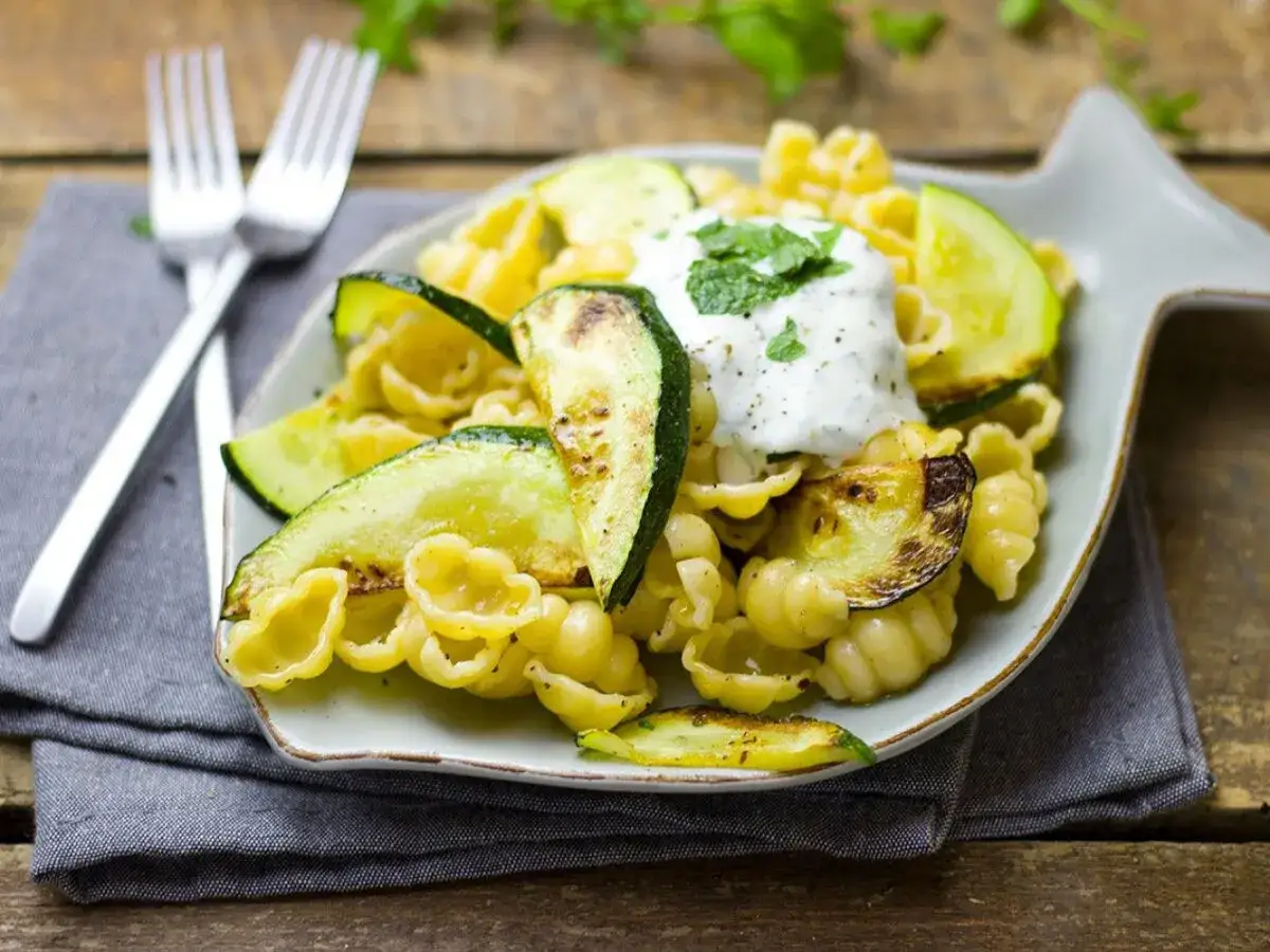 Piatto di pasta con zucchine grigliate, condita con una salsa cremosa e erbe aromatiche. Un piatto leggero e gustoso.