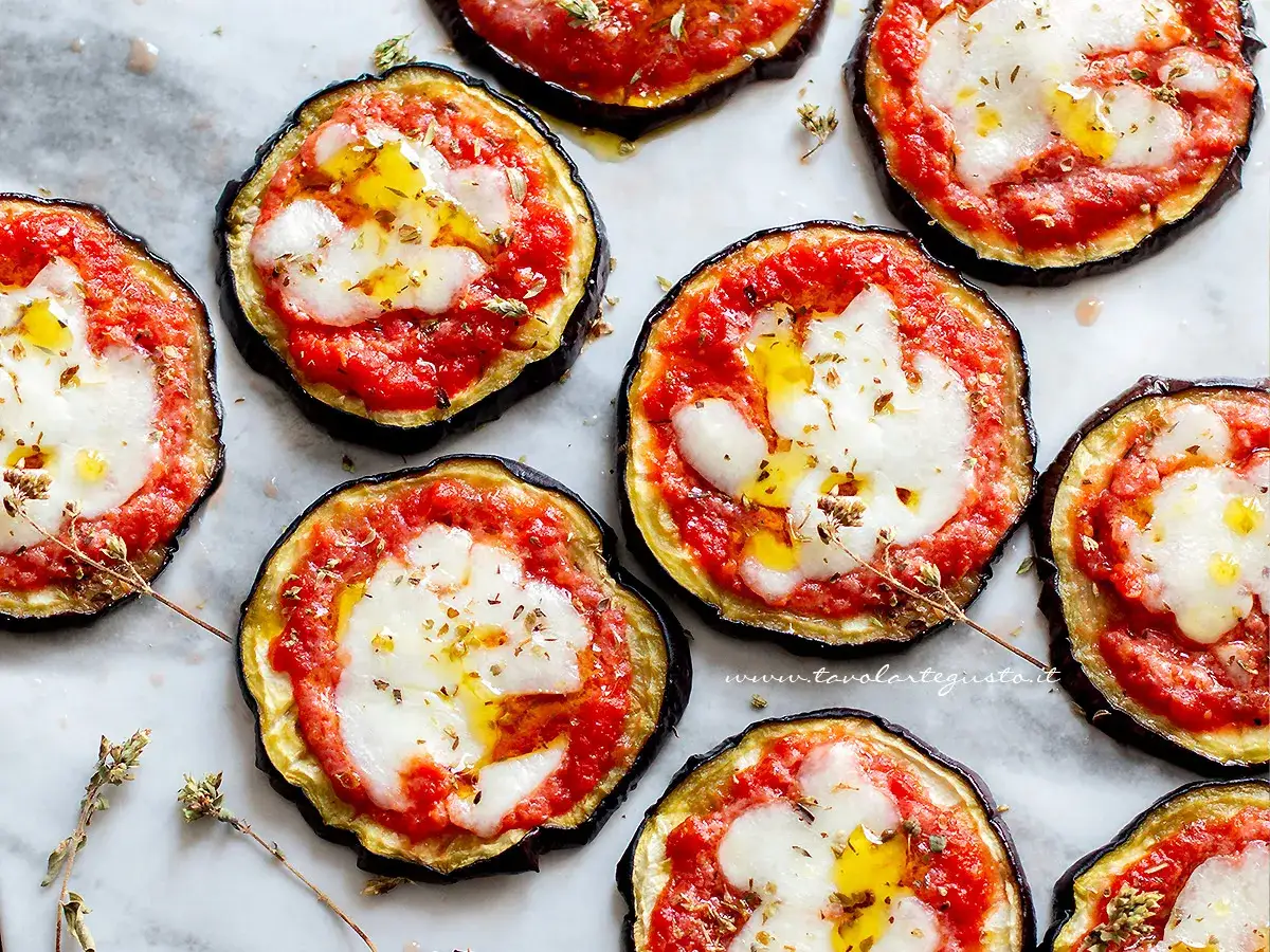 Pizzette di melanzane al forno, gustose e leggere, con pomodoro, mozzarella filante e un filo d'olio.