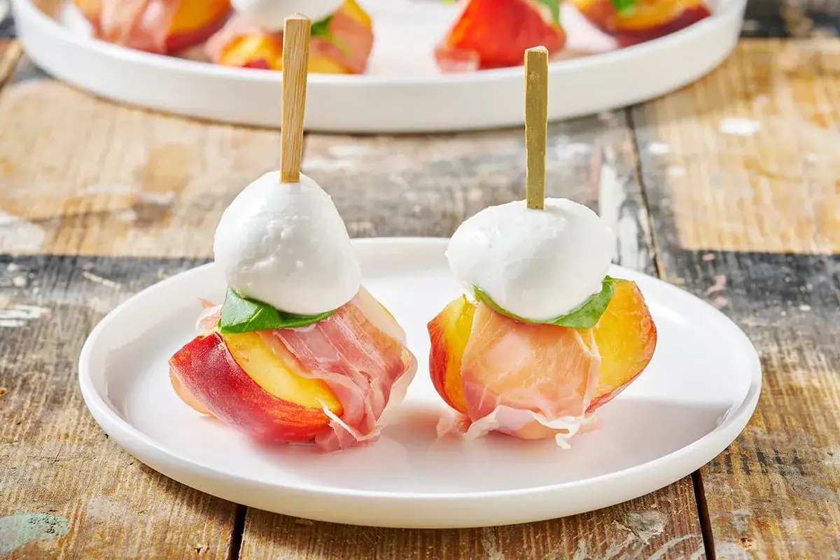 Spiedini con pesche, prosciutto crudo, mozzarella e basilico, perfetti antipasti estivi.
