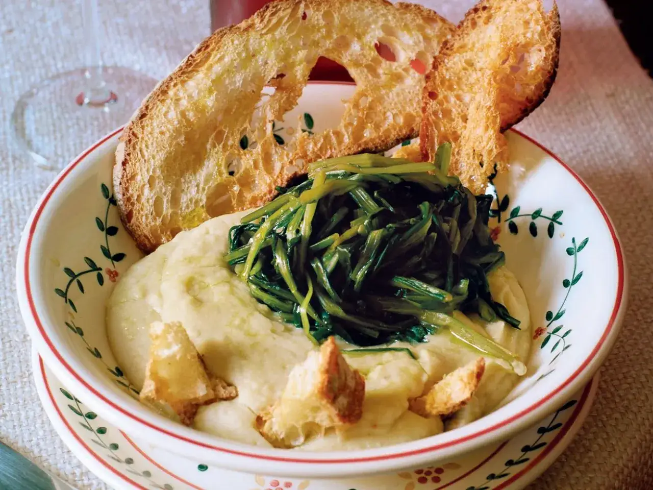 Fave e cicoria in una ciotola decorata, con crostini di pane abbrustolito.