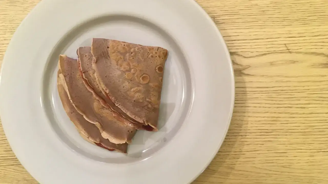 Tre crepes piegate su un piatto bianco, con un ripieno rossastro visibile. Una deliziosa crepes ricetta senza burro, perfetta per una colazione leggera.
