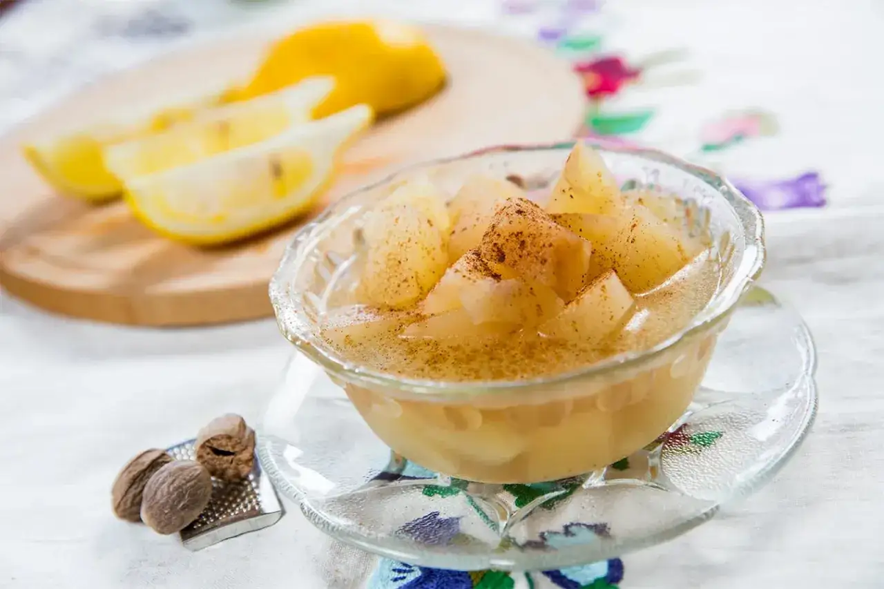 Mele cotte in pentola, dolci e profumate, servite in una ciotola di vetro con cannella e limone a fette sullo sfondo.