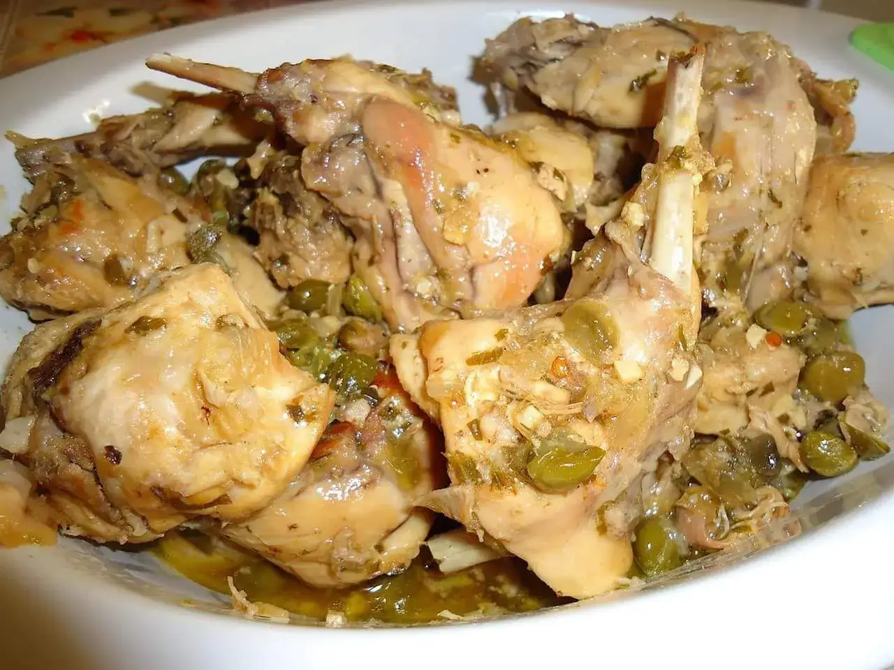 Piatto fumante di coniglio alla cacciatora in bianco, con olive verdi e erbe aromatiche. Un classico della cucina italiana.