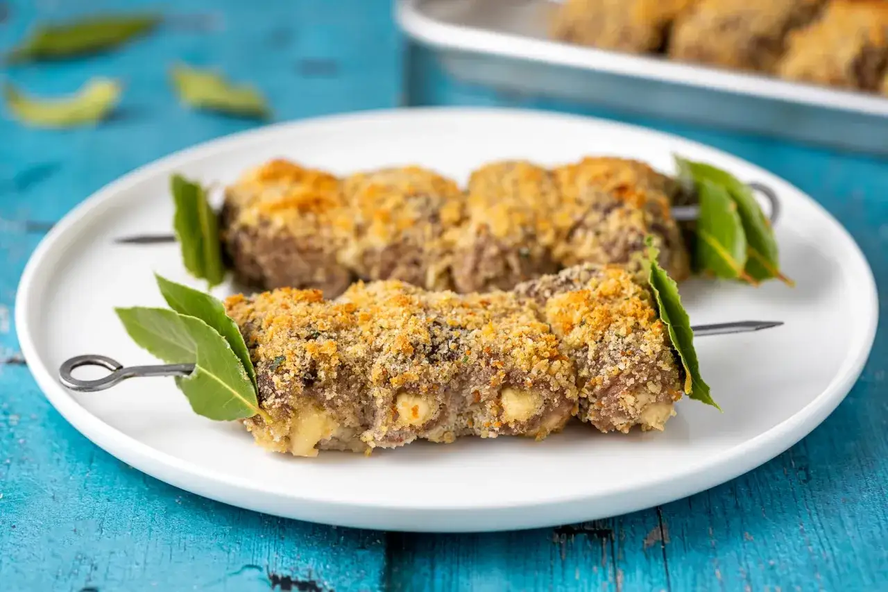 Involtini alla messinese su spiedini, impanati e dorati, guarniti con foglie di alloro.