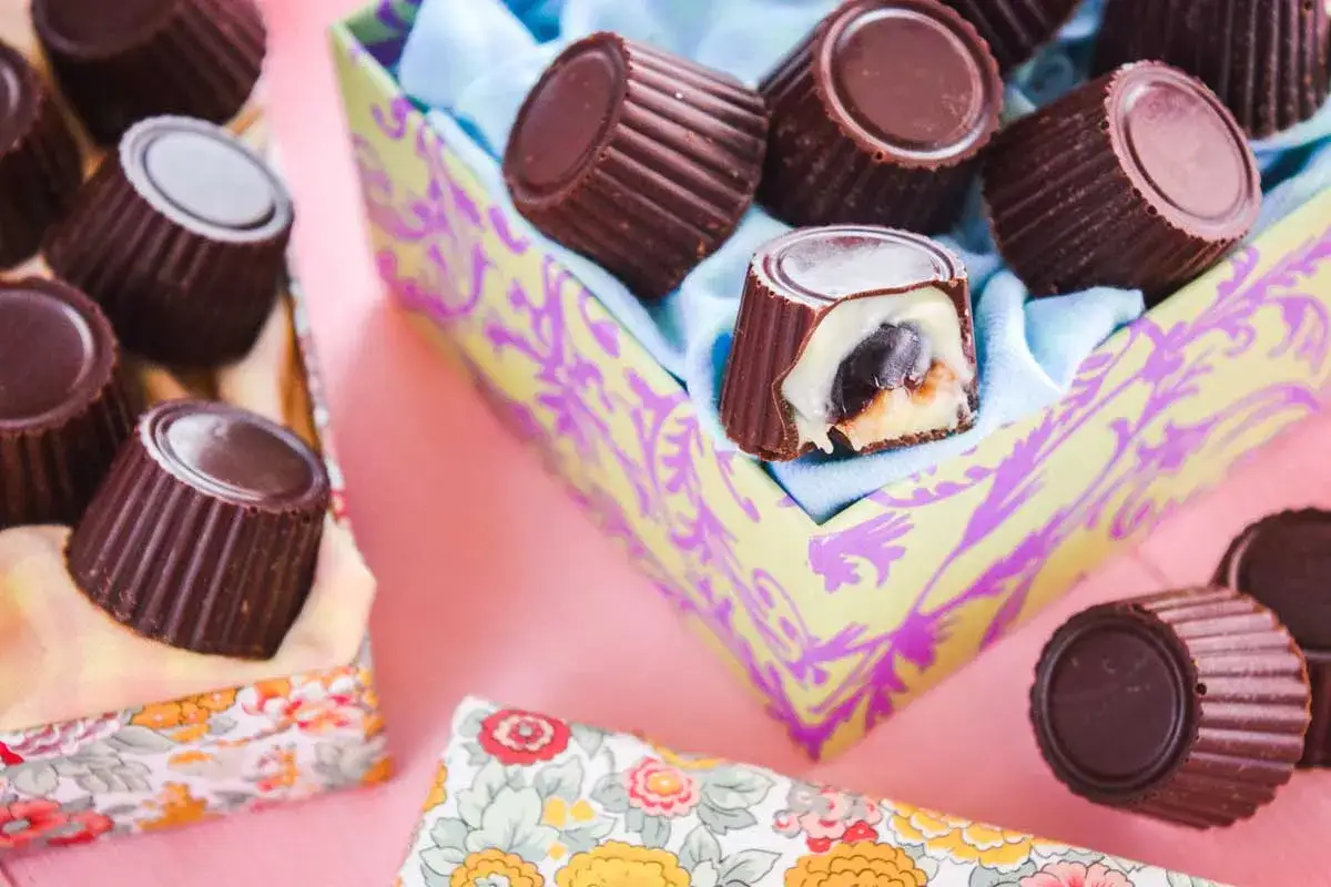 Deliziosi cioccolatini fatti in casa, alcuni con ripieno cremoso e ciliegia, presentati in un vassoio decorato.