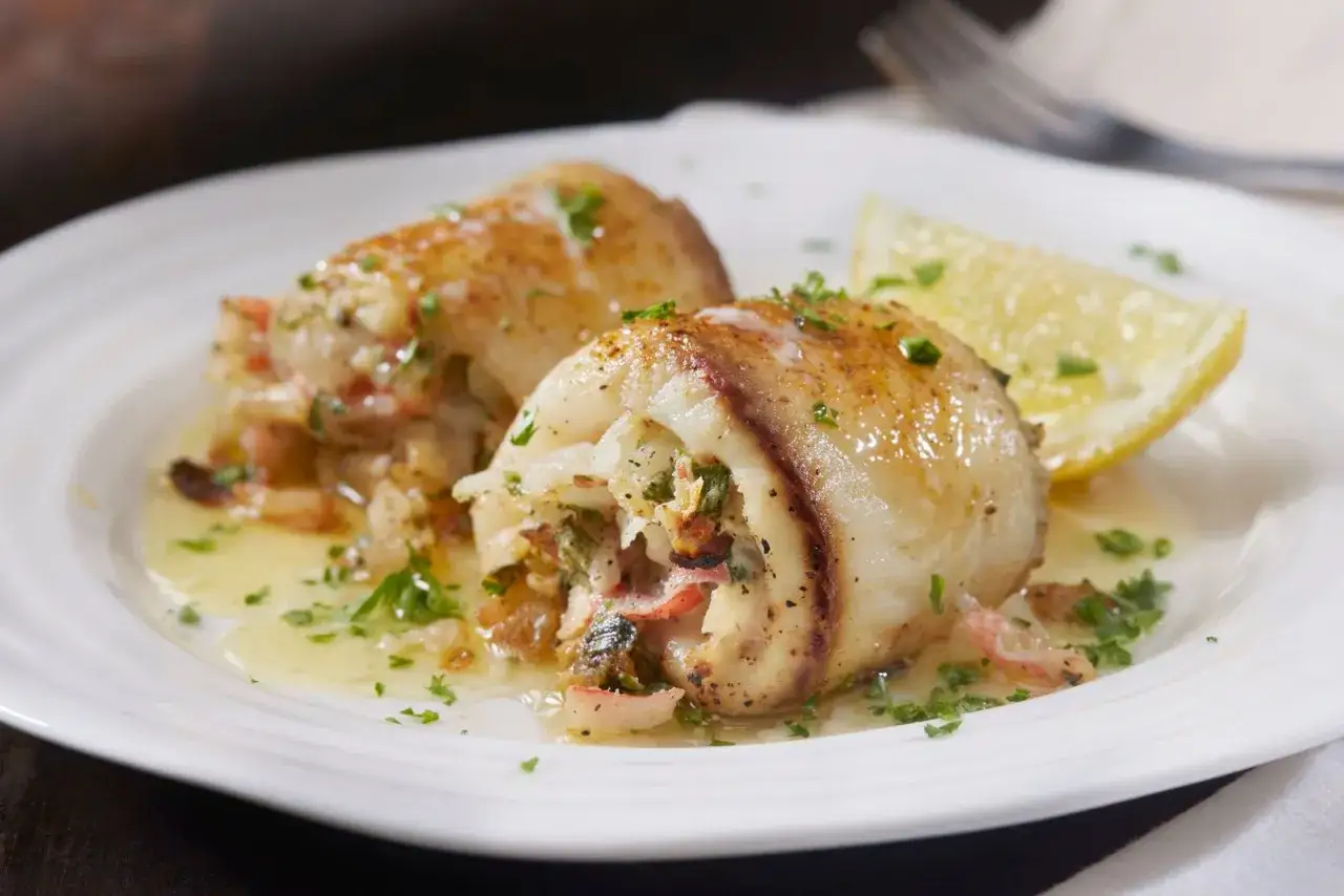 Deliziosi involtini di pesce spada ripieni, serviti su un piatto bianco con una fetta di limone e prezzemolo tritato.