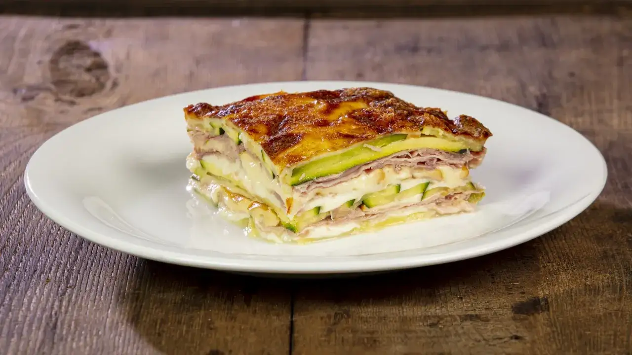 Una fetta di parmigiana di zucchine alla siciliana, stratificata con zucchine, prosciutto e formaggio filante, gratinata in forno.
