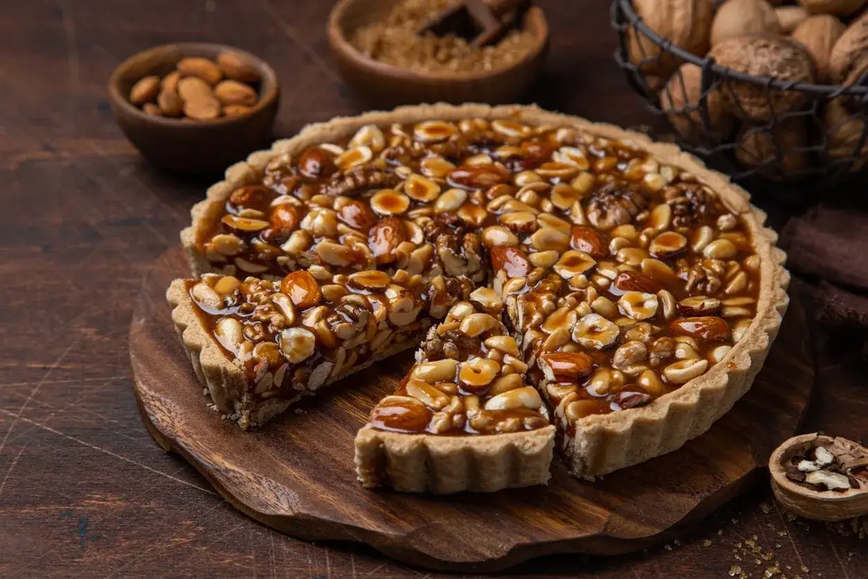Torta croccante con un ripieno generoso di nocciole e mandorle caramellate. Un vero piacere per gli amanti dei dolci con nocciole.