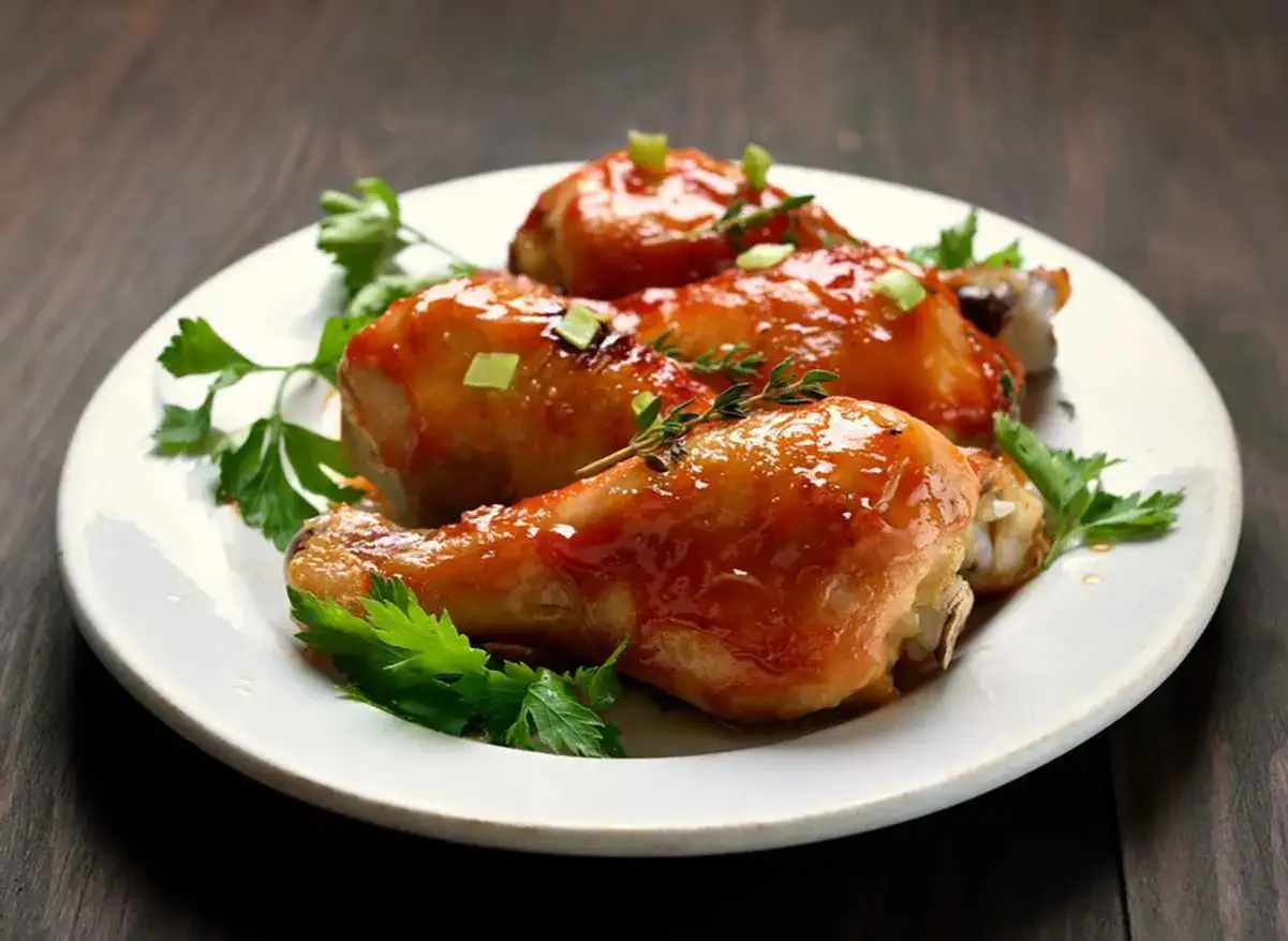 Tre cosce di pollo glassate, guarnite con prezzemolo e erbe aromatiche, pronte per essere gustate. Un delizioso pollo alla birra in padella.