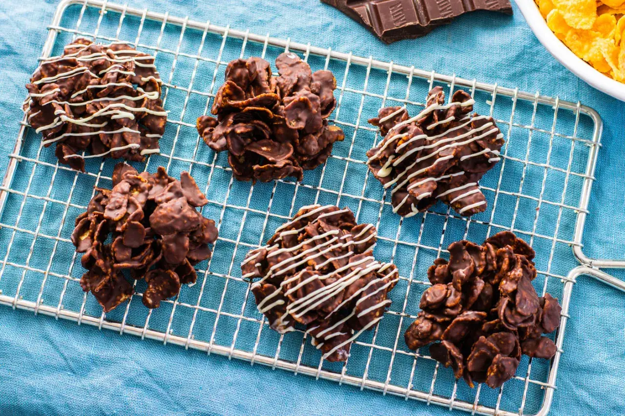 Sei deliziosi biscotti corn flakes e cioccolato, alcuni decorati con cioccolato bianco, riposano su una griglia.