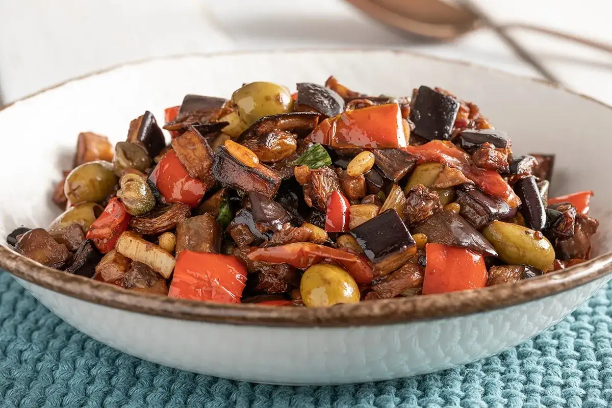 Caponata ricetta: melanzane, peperoni, olive e capperi in un piatto invitante.