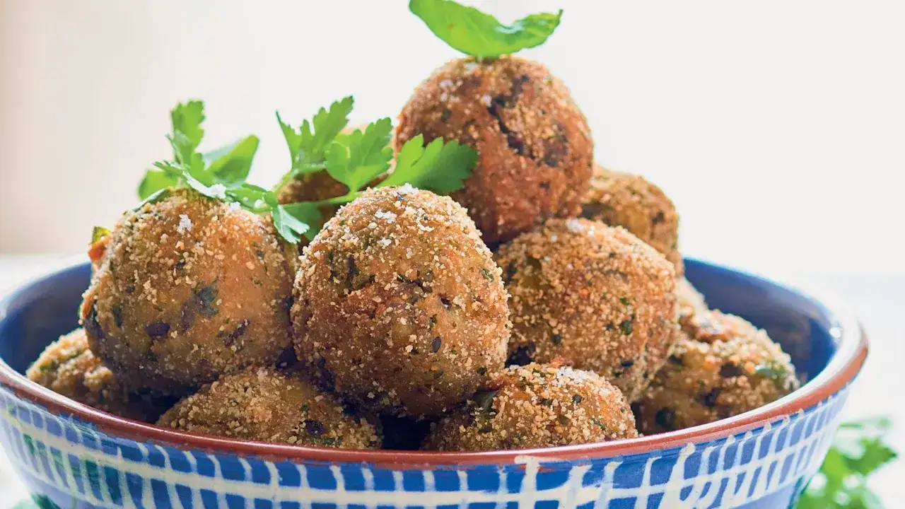 Polpette di melanzane dorate e croccanti, guarnite con prezzemolo fresco e basilico, servite in una ciotola blu.