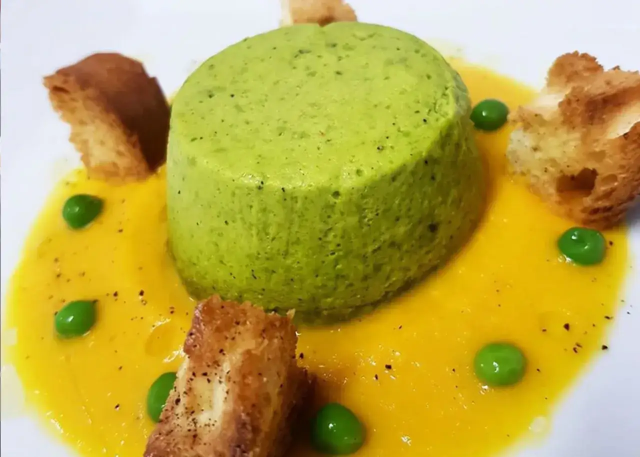 Sformato di piselli verde brillante su vellutata gialla, guarnito con piselli freschi e crostini dorati.