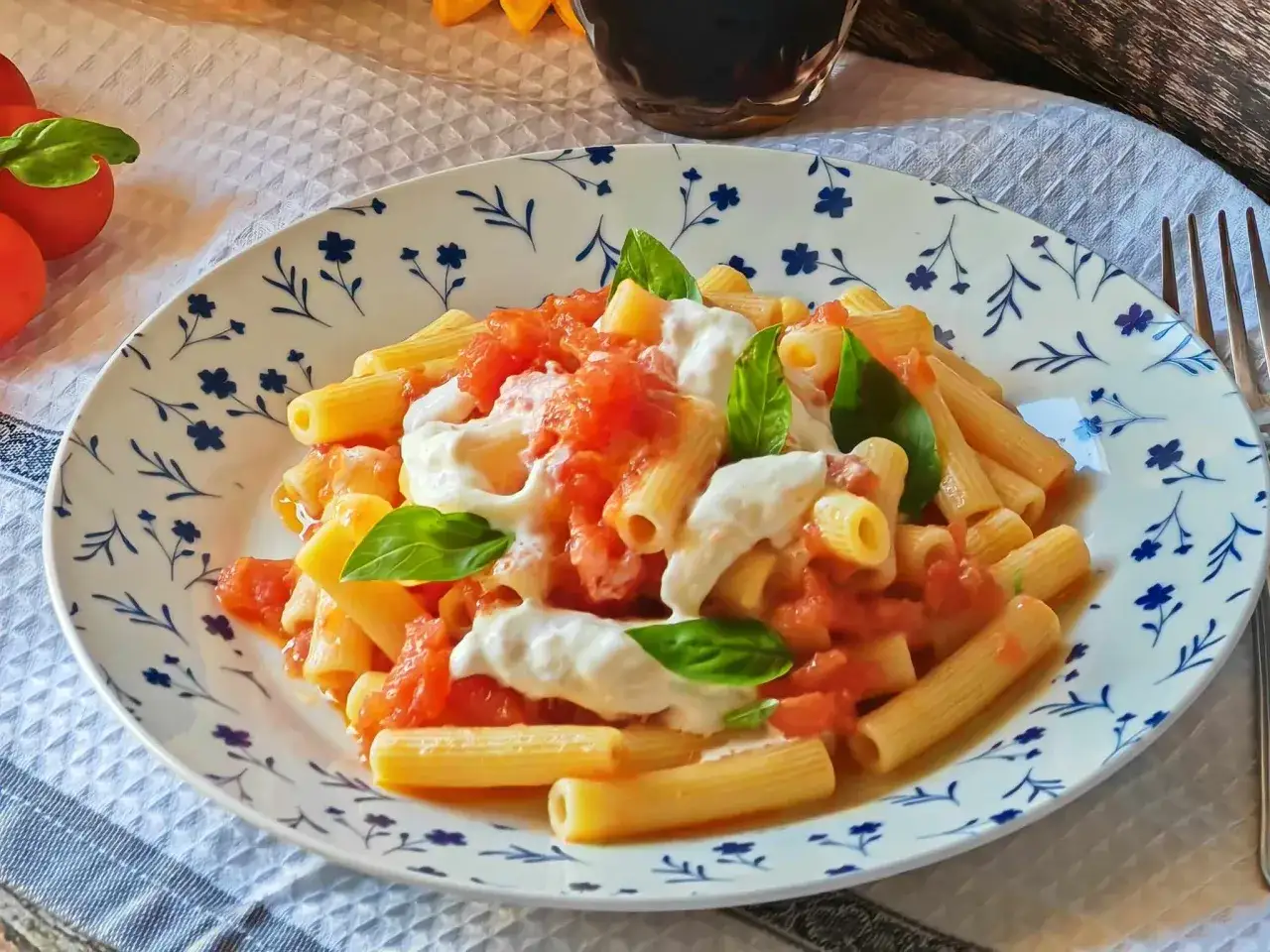 Piatto di pasta con sugo di pomodoro fresco e abbondante stracciatella, guarnito con foglie di basilico.