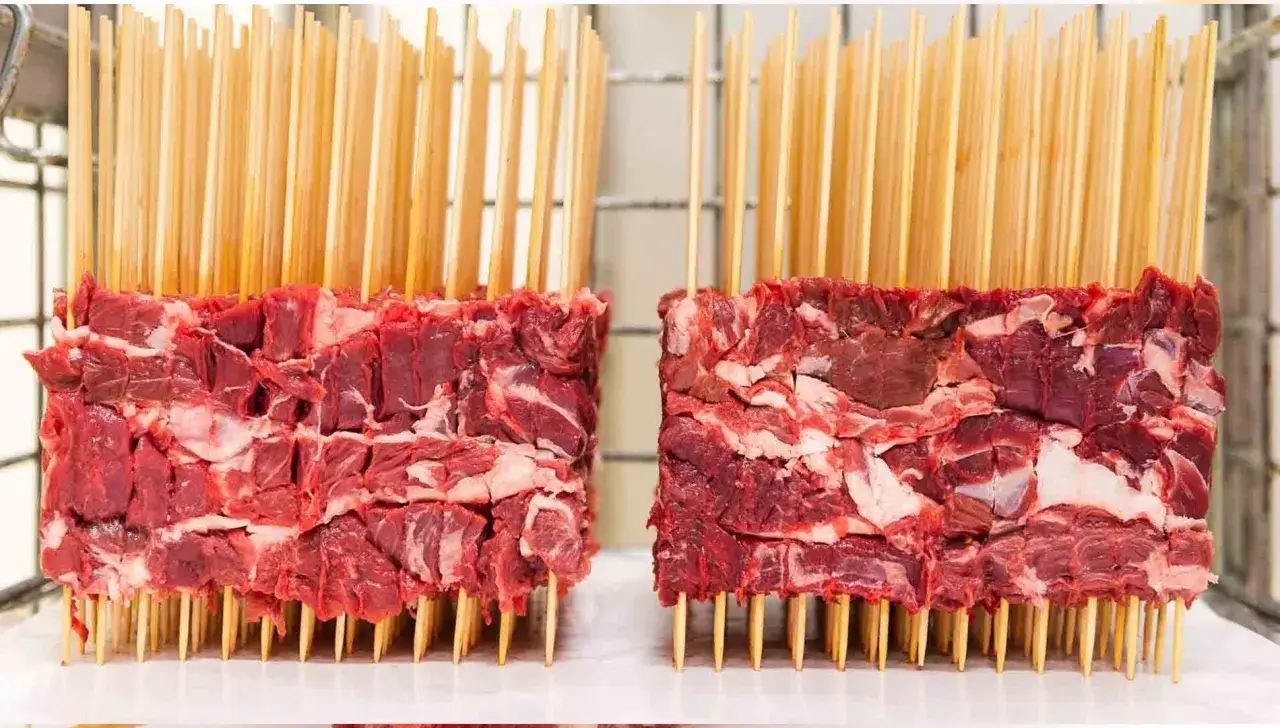 Due blocchi di carne cruda, pronti per diventare succulenti arrosticini al forno, infilzati su spiedini di legno.