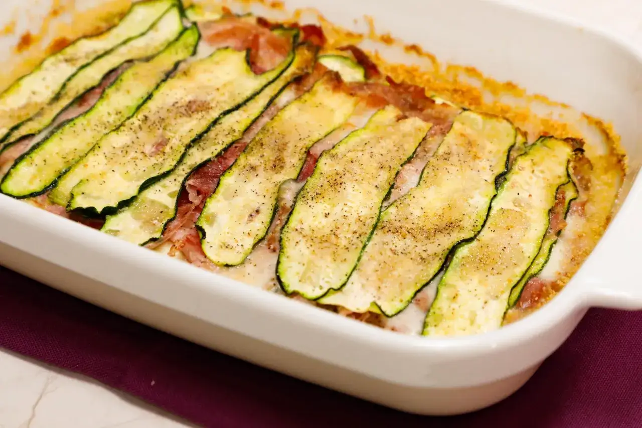 Sformato di zucchine appena sfornato, con fette sottili di zucchina grigliata e prosciutto, cosparso di pepe nero.