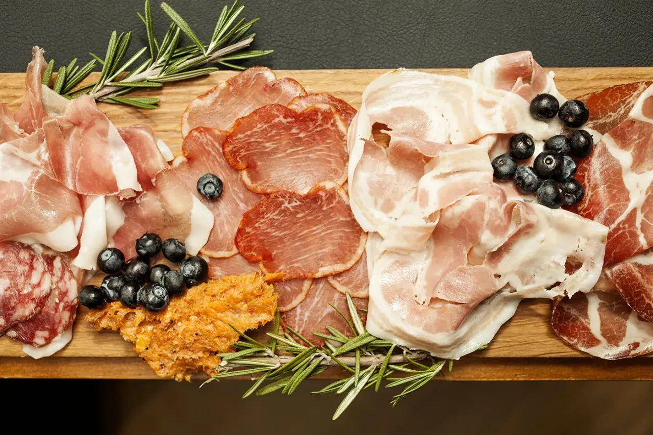 Un invitante tagliere salumi e formaggi, con fette sottili di prosciutto, coppa, pancetta, salame, mirtilli e rosmarino.
