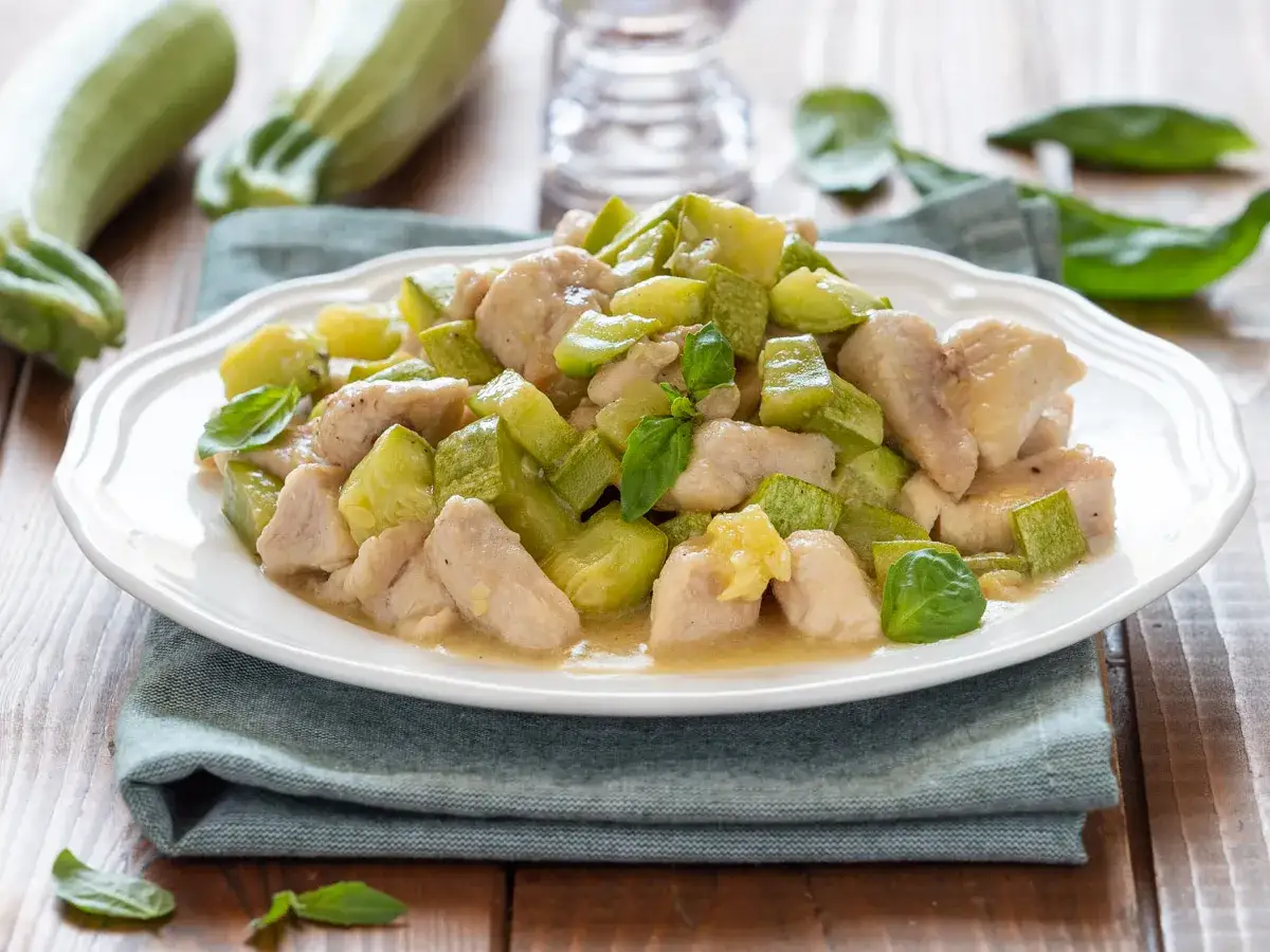 Un saporito piatto di pollo e zucchine, condito con basilico fresco, servito su un piatto bianco.