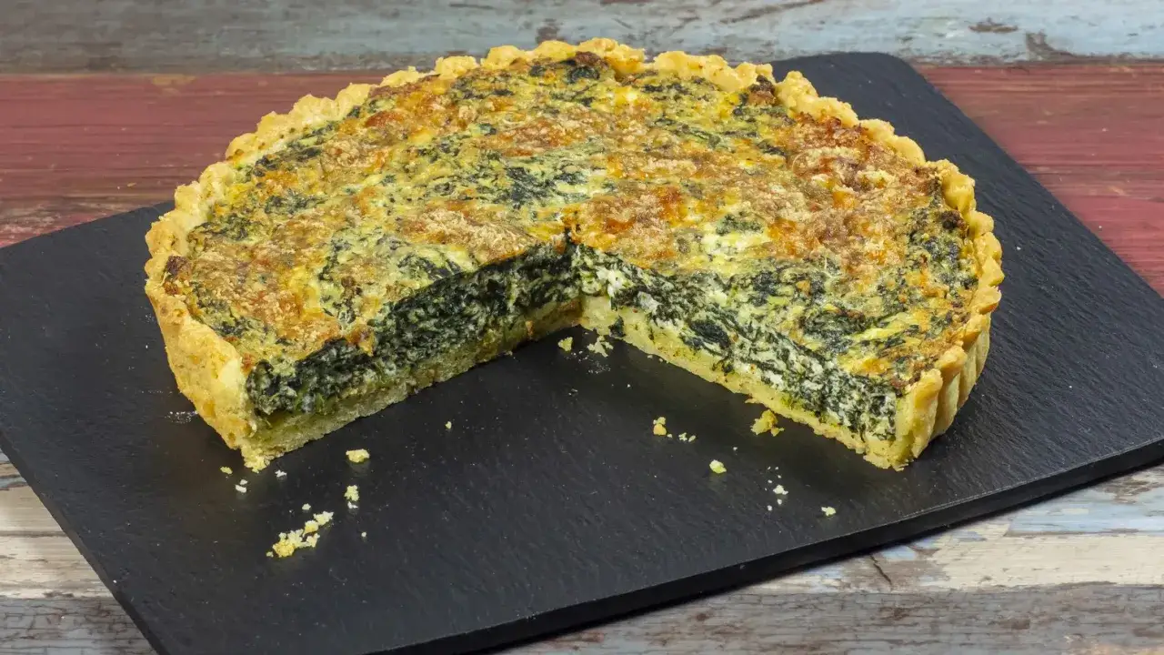 Una fetta di torta salata ricotta e spinaci, con crosta dorata e ripieno cremoso, su una pietra scura.