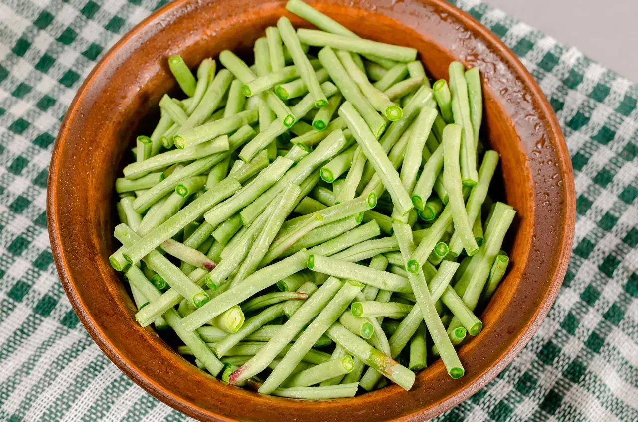 Fagiolini freschi, tagliati e pronti per essere cucinati in umido, in una ciotola di terracotta su una tovaglia a quadri verdi.