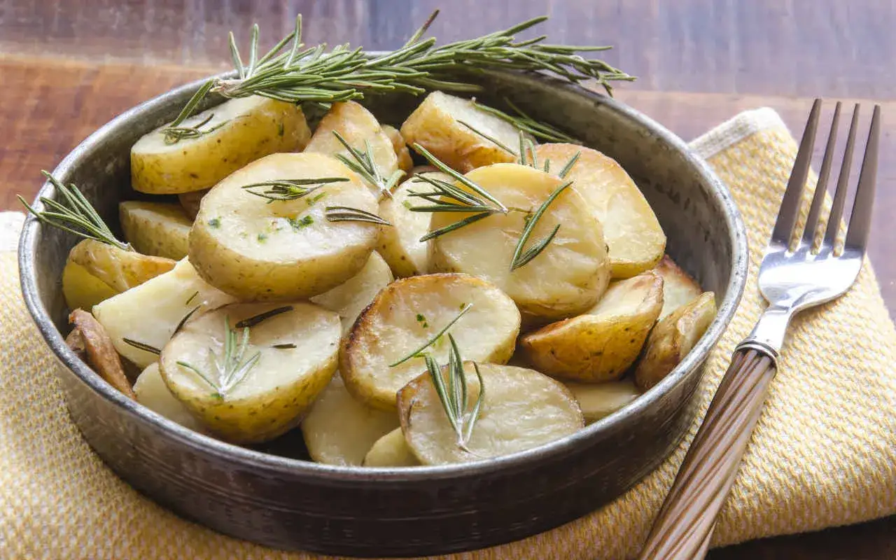 Patate dolci in padella, dorate e profumate al rosmarino, servite in una ciotola di metallo con una forchetta accanto.