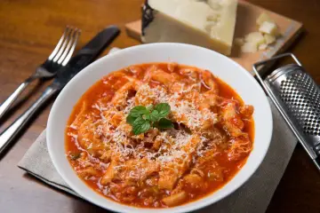 Un piatto fumante di trippa alla romana, cosparso di formaggio grattugiato e guarnito con menta fresca. Accanto, una grattugia e un pezzo di formaggio.