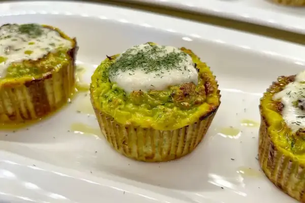 Tre tortini di zucchine dorati, guarniti con formaggio fuso e aneto, serviti su un piatto bianco.