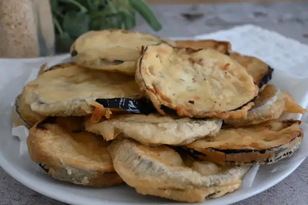 Piatto di melanzane fritte pastellate, dorate e croccanti, pronte per essere gustate.