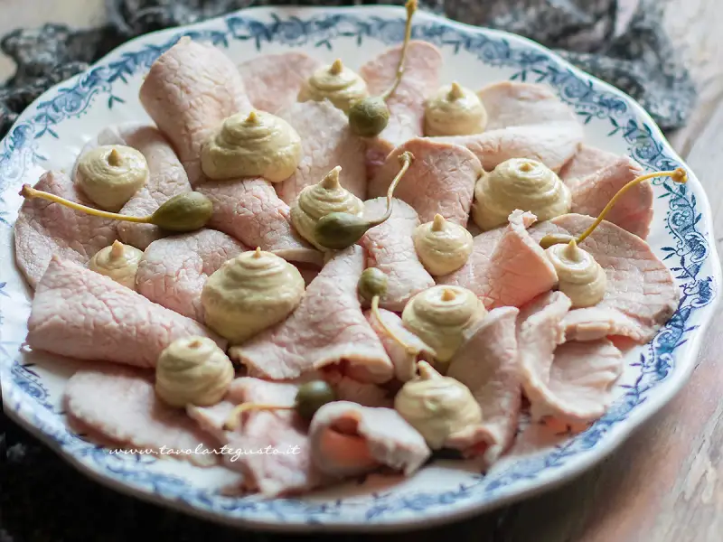 Piatto di vitello tonnato con salsa cremosa, capperi e guarnizioni.