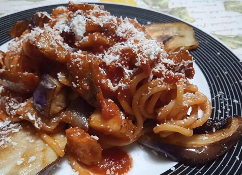 Un piatto invitante di pasta alla norma con melanzane fritte, sugo di pomodoro e ricotta salata grattugiata.